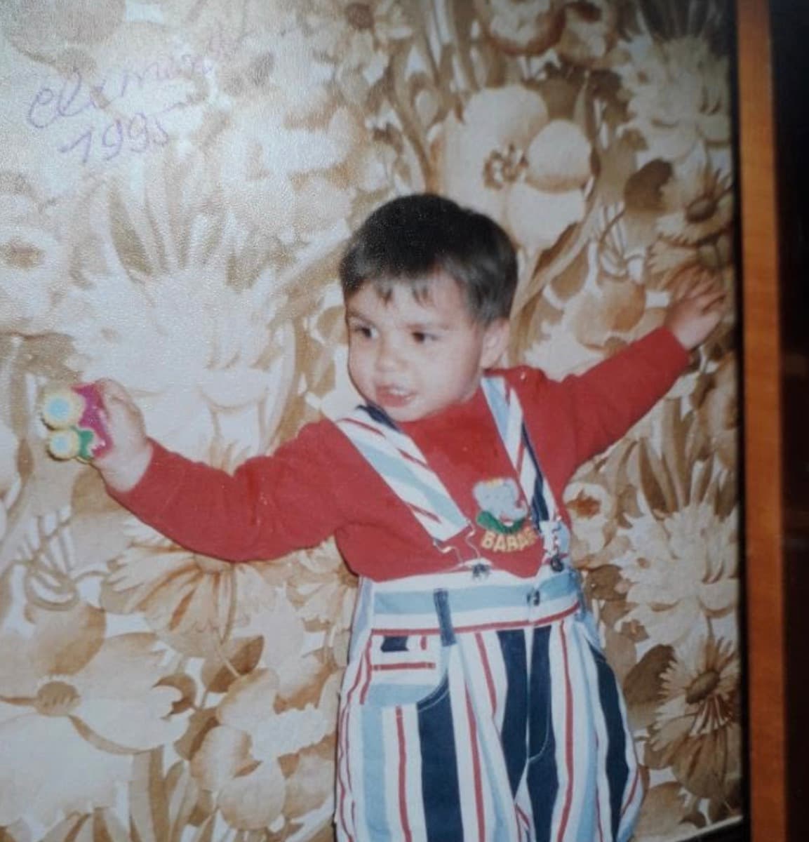 Clément as a child, in striped overalls, holding a toy