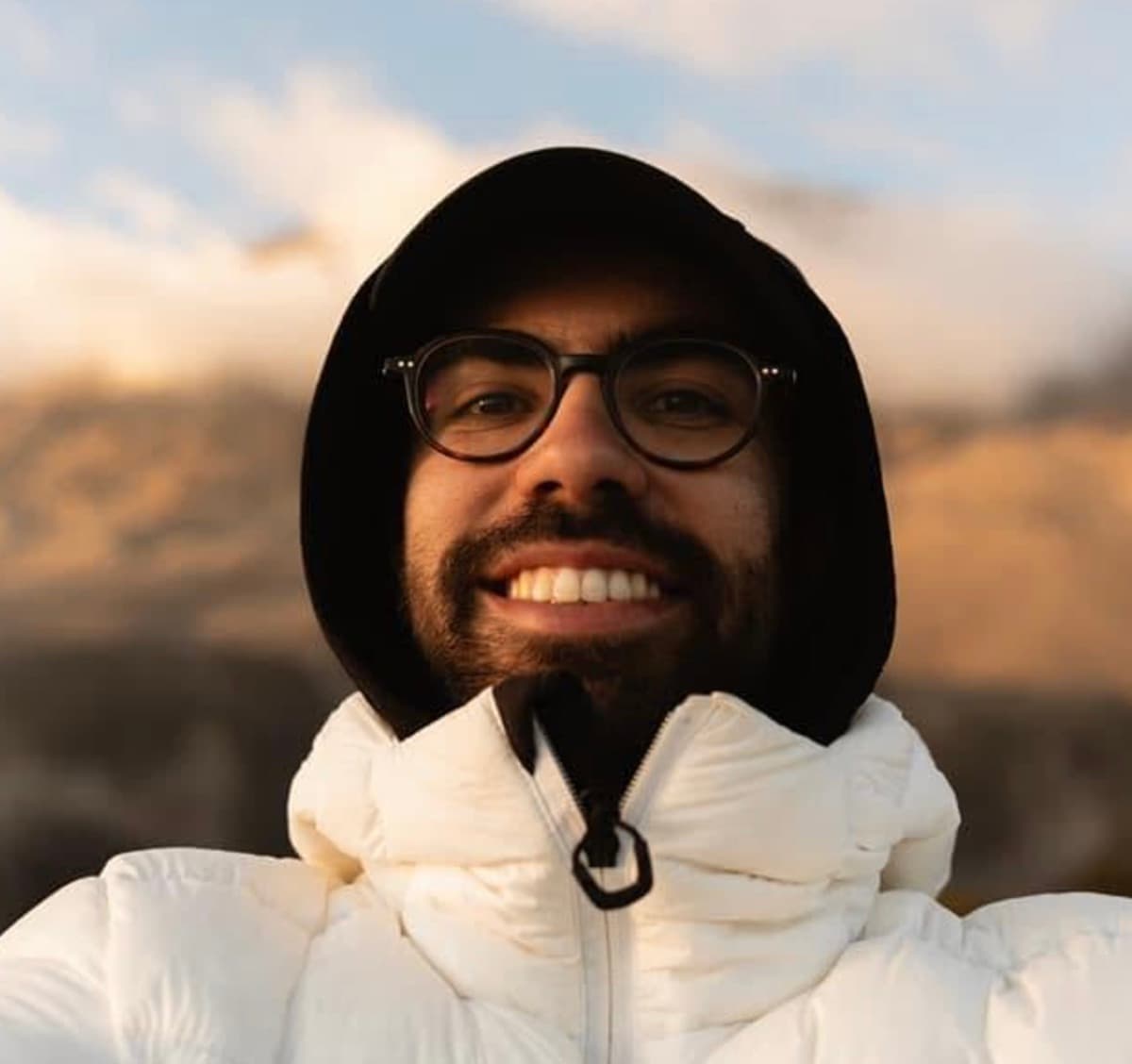 Clément in a black hoodie, smiling against a sunset